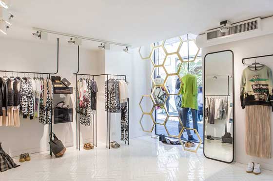 Interno del flagship store Alysi a Roma con arredi minimal, reticolo in ottone e abiti esposti su strutture metalliche
