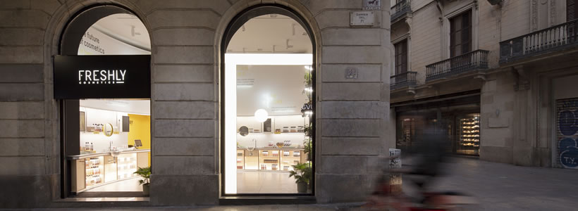 Facciata esterna del negozio Freshly Cosmetic a Barcellona, con ampie vetrine e logo illuminato di sera.