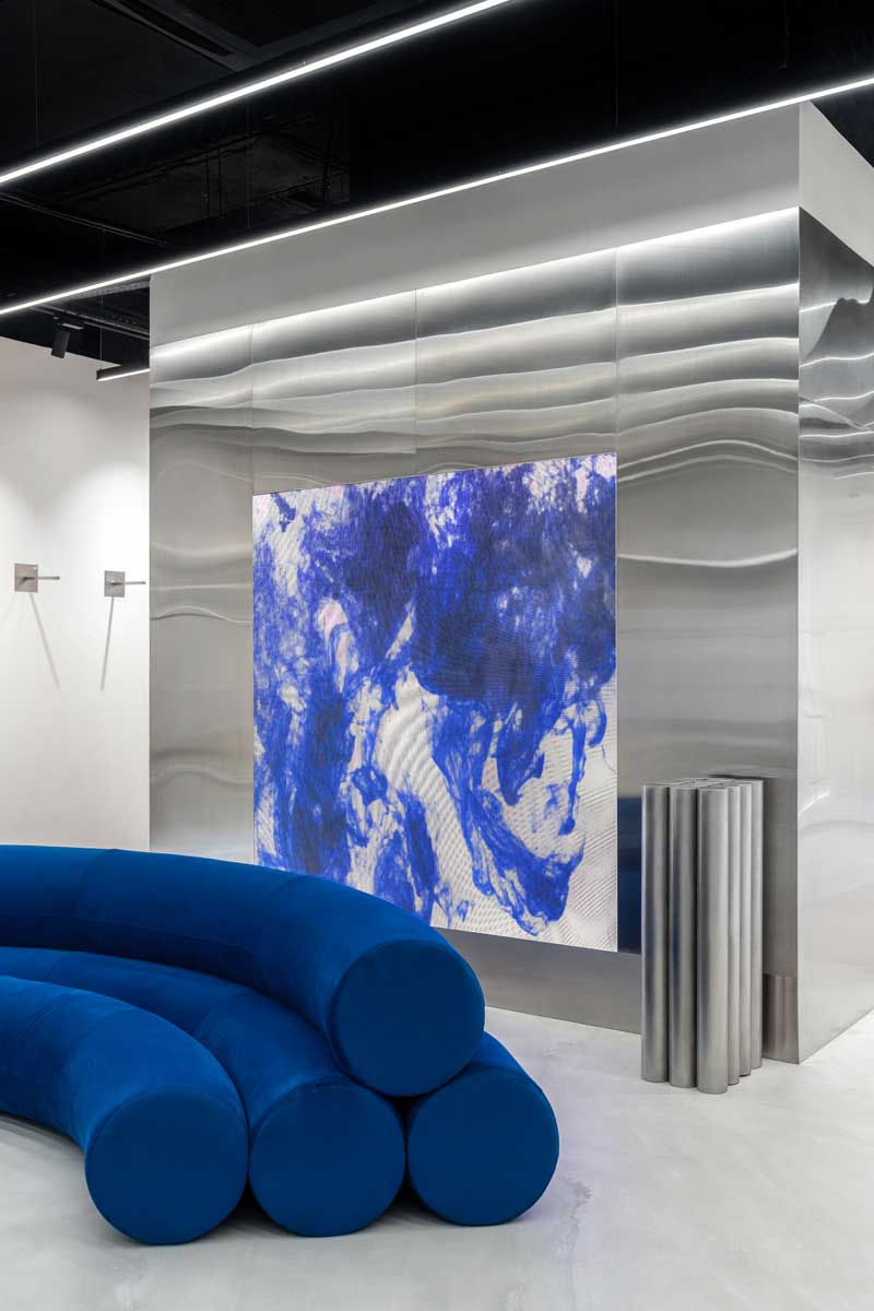 Zona living showroom Cher’17 con divano cilindrico blu e schermo LED
