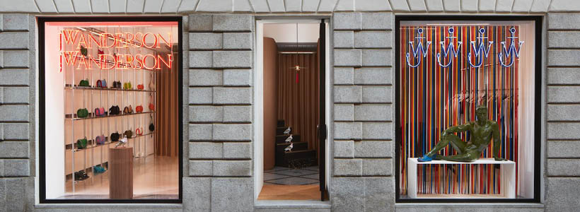 Facciata del negozio di JW Anderson a Milano con vetrine a tutta altezza e insegna al neon nel Quadrilatero della moda