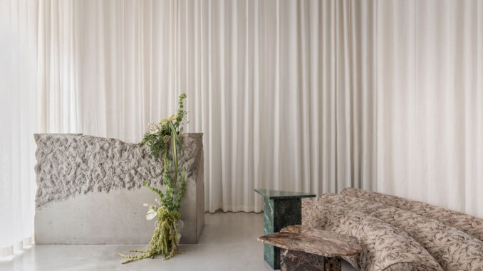 Raw concrete reception desk with textured surface, full-height white curtains and curved gobelin sofa at Stan yoga and barre studio in Kyiv
