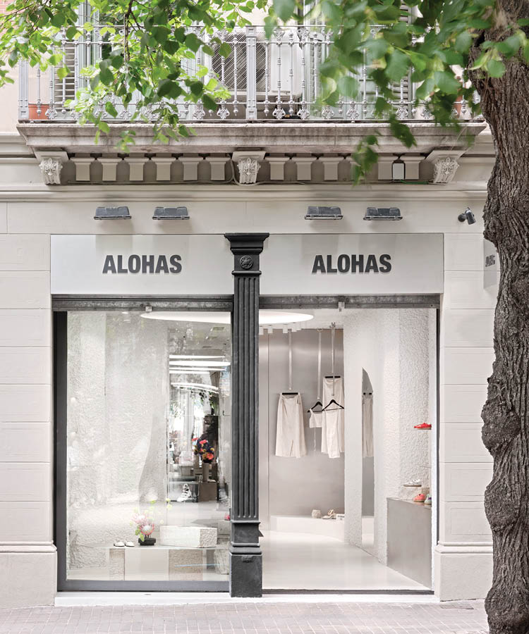 Storefront and display windows of the Alohas flagship store in Barcelona with signage on a light facade and a view into the textured white interior