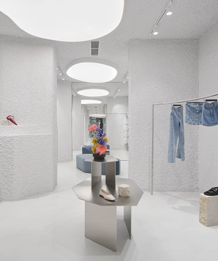 Interior of the Alohas flagship store in Barcelona with textured white walls, large circular ceiling lights, a metal display table, and denim garments on a rail
