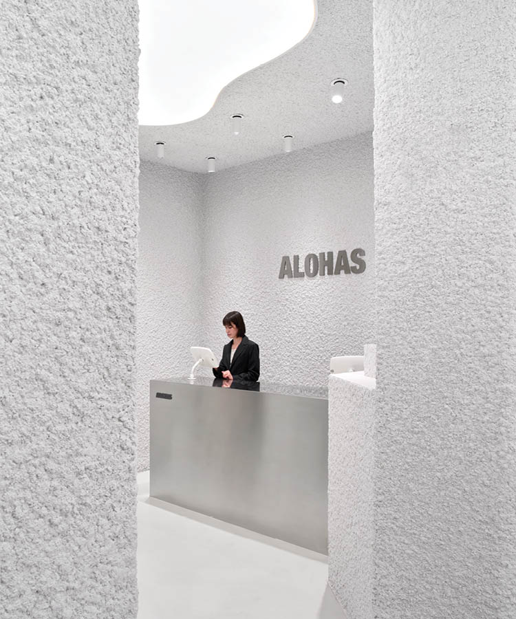 Reception area of the Alohas flagship store in Barcelona with textured white walls, wall signage, and a satin metal counter