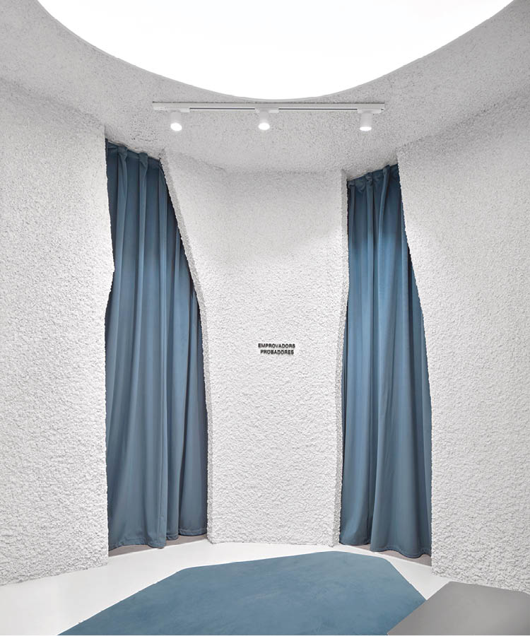 Fitting room area in the Alohas flagship store in Barcelona with textured white walls, blue curtains, and track lighting
