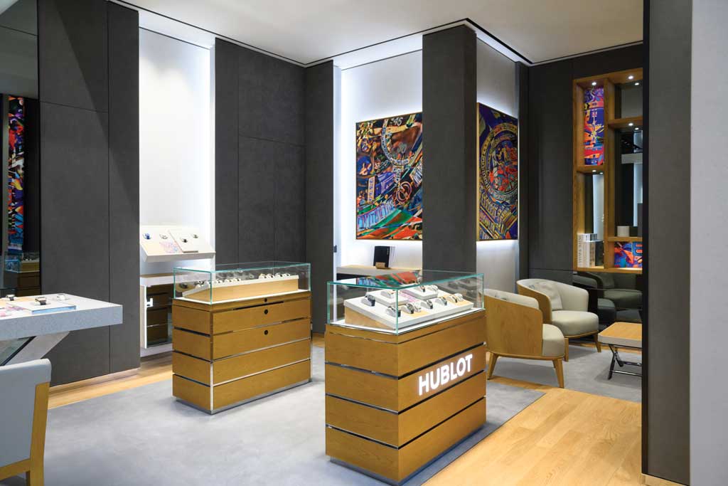 Display showcases and lounge area of the Hublot boutique at Marina Bay Sands in Singapore with glass cases on wood bases and wall art