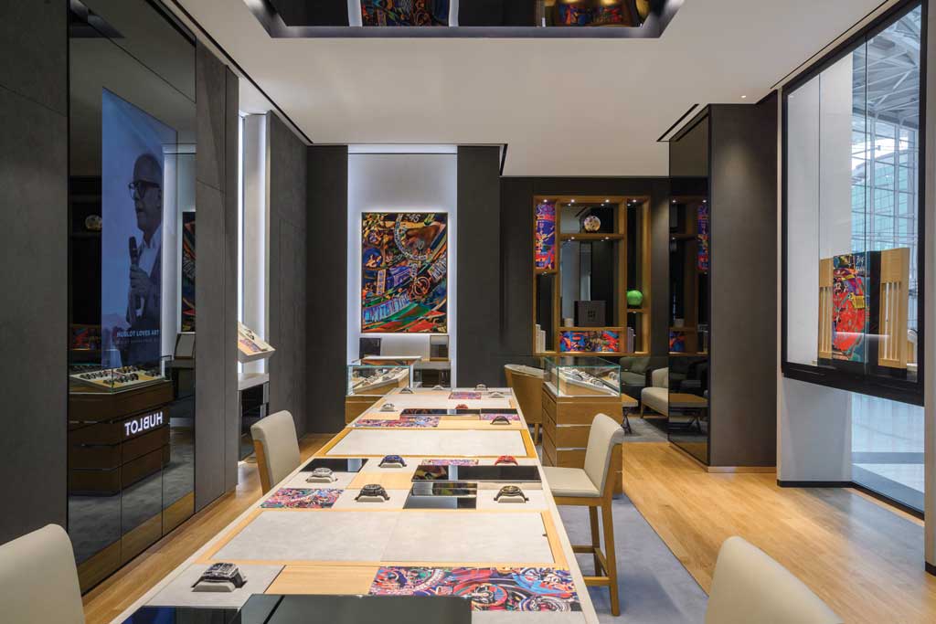 Consultation table and interior pathway of the Hublot boutique at Marina Bay Sands in Singapore with dark wall panels, wood inserts, and watch showcases