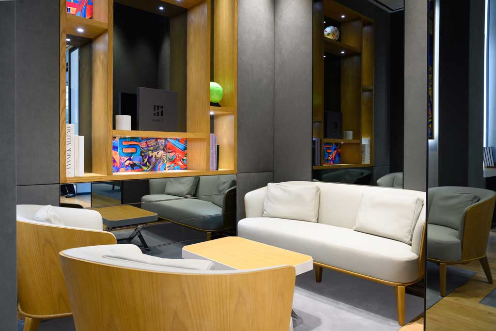 Lounge area of the Hublot boutique at Marina Bay Sands in Singapore with a sofa, armchairs, and a backlit wood shelving unit