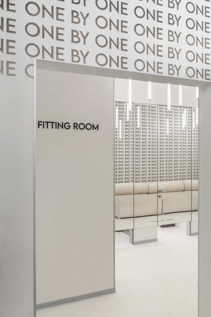 Ingresso dei camerini nello showroom One By One con scritta “Fitting Room”, pannelli specchiati e grafica tipografica a parete