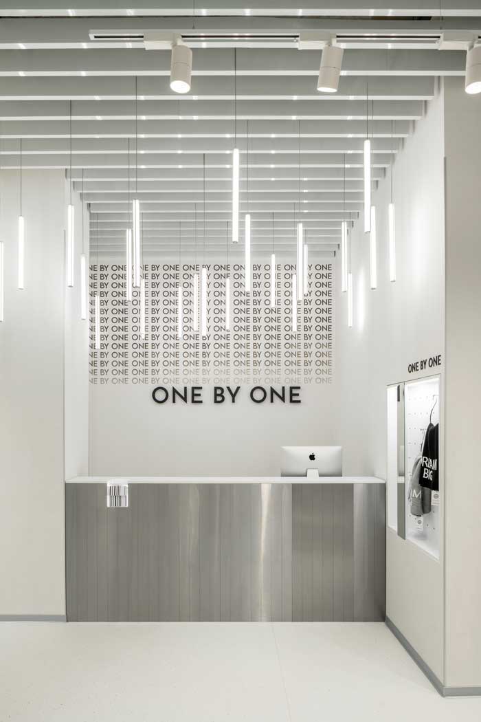 Banco cassa dello showroom One By One con rivestimento metallico, logo a parete e corpi illuminanti sospesi