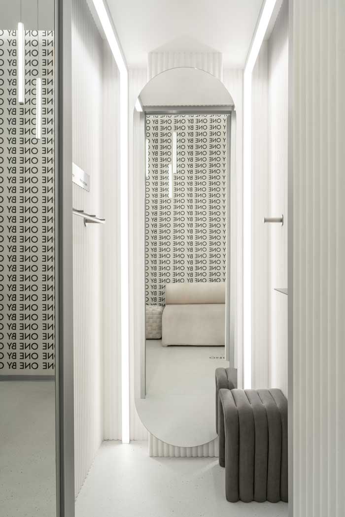 Corridoio dei camerini nello showroom One By One con pareti scanalate, specchio ad arco e luci lineari a LED