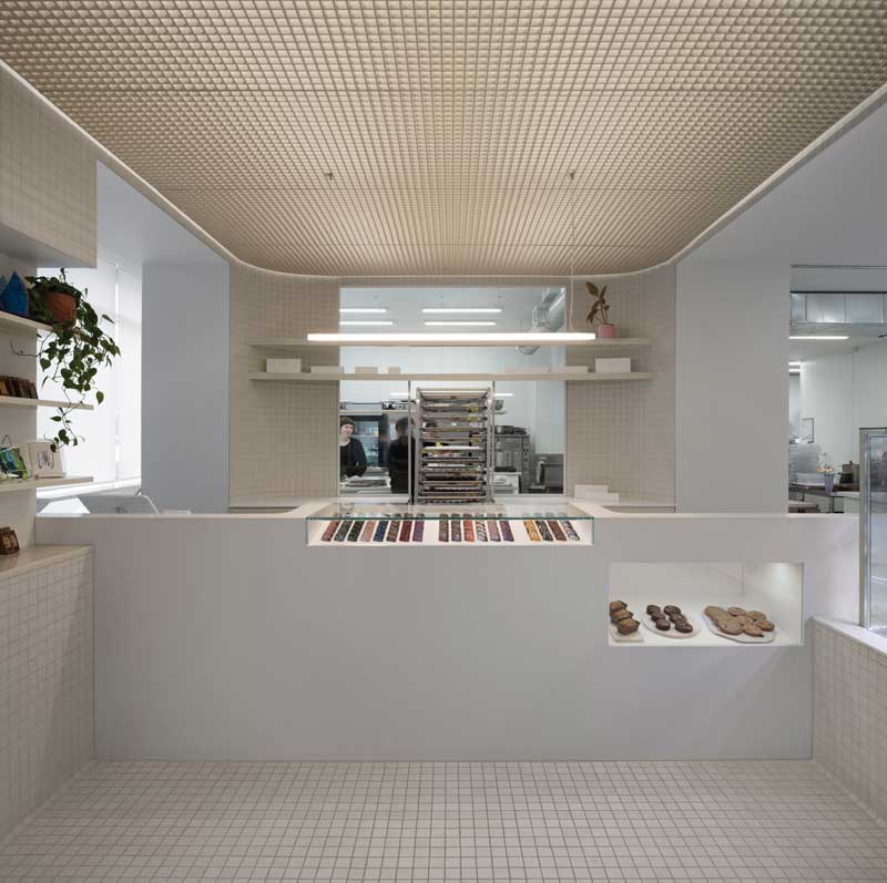 Interno di una pasticceria dal design minimalista e moderno, con una grande vetrina centrale che espone una selezione ordinata di dolci colorati.