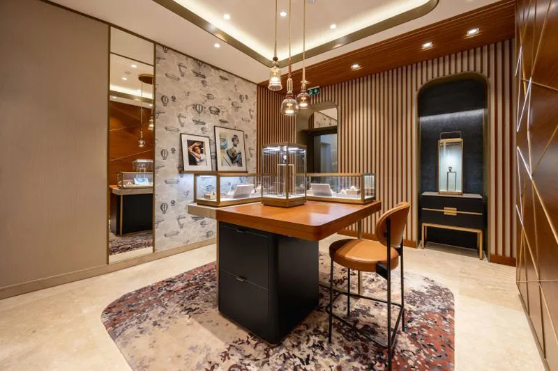 Interno della boutique Vacheron Constantin a Roma, con espositori di orologi illuminati, carta da parati Fornasetti a tema mongolfiere e dettagli di design in legno e metallo