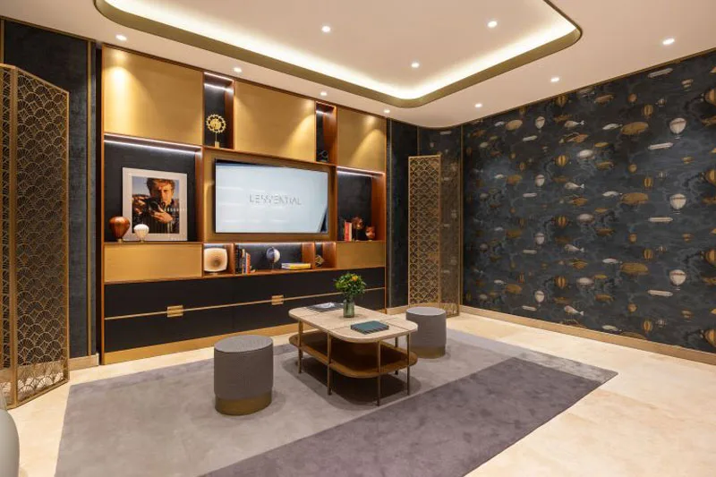 VIP Lounge della boutique Vacheron Constantin a Roma, con pareti decorate da carta da parati Fornasetti a tema blu, mobili eleganti in legno e metallo, tavolino centrale e schermo incastonato in una libreria illuminata.
