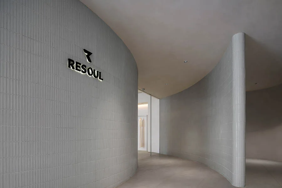 Ingresso di un concept store con pareti curve rivestite in piastrelle minimaliste grigie, logo illuminato 'RESOUL' e un design moderno e raffinato