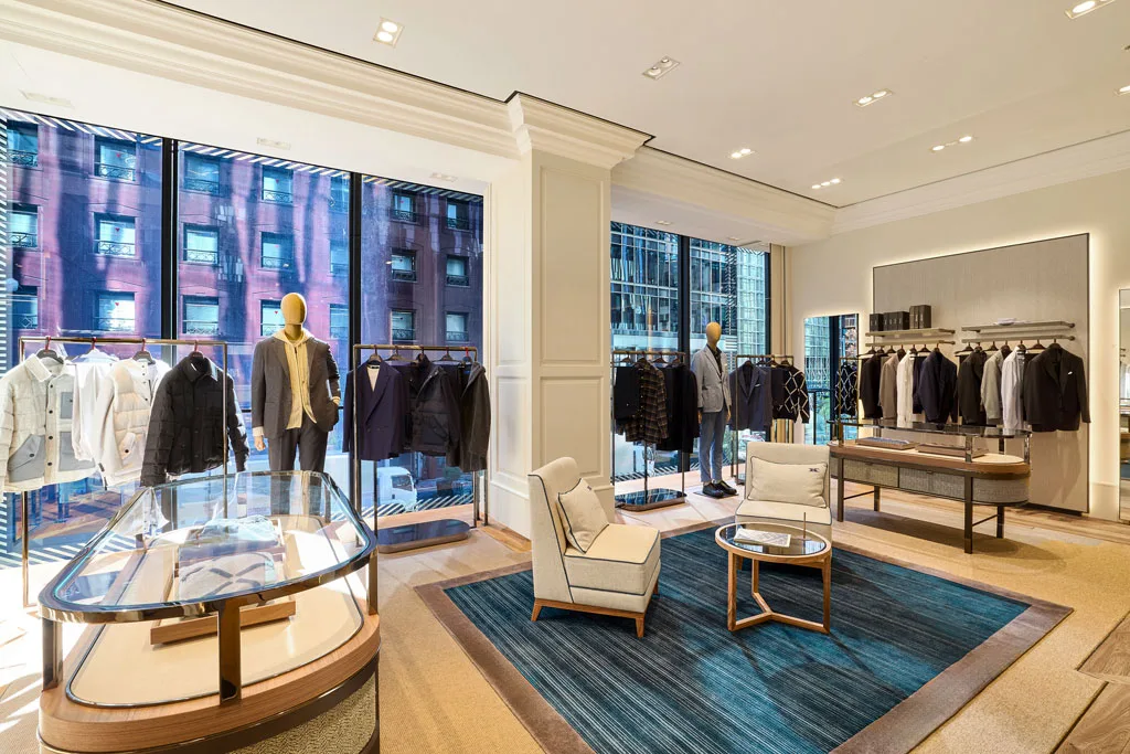 Vista interna del flagship store Kiton a Ginza, Tokyo, con ampie vetrate che inondano di luce naturale l'ambiente. Espositori eleganti e arredi su misura creano un'atmosfera di quiet luxury