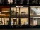 Facciata del flagship store Kiton a Ginza, Tokyo, con design trasparente e minimale, accanto ai brand di lusso Strasburgo ed Emporio Armani. L'eleganza architettonica risalta nel cuore del quartiere del lusso