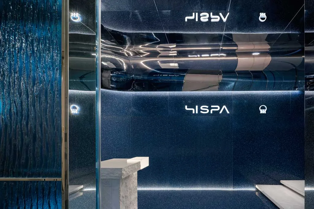 Ingresso blu della SPA HISPA con corridoio illuminato e facciata in vetro ondulato.