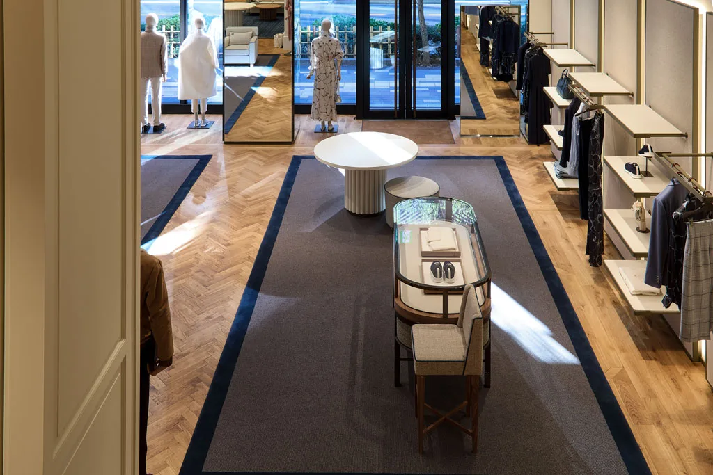 Interno del flagship store Kiton a Ginza, Tokyo, con pavimento in legno a spina di pesce, arredi minimalisti e dettagli eleganti. Il design curato offre un’esperienza di shopping sofisticata e rilassante.