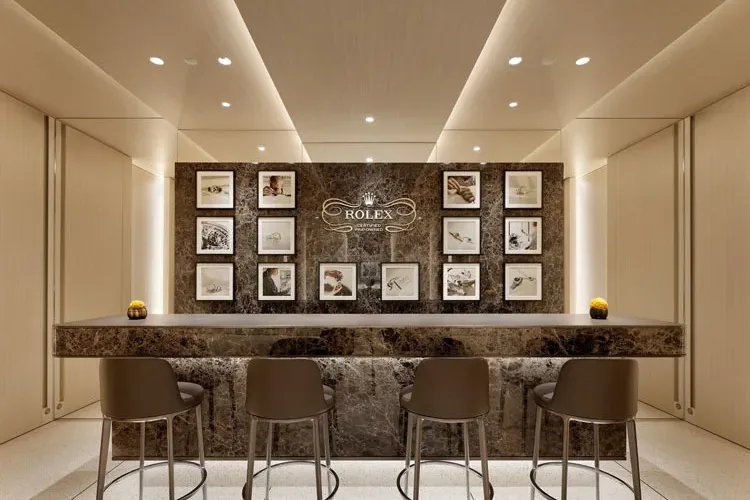 Lounge esclusiva nel flagship store Rolex Omotesando a Tokyo, con bancone in marmo scuro e parete decorata con immagini iconiche del brand.