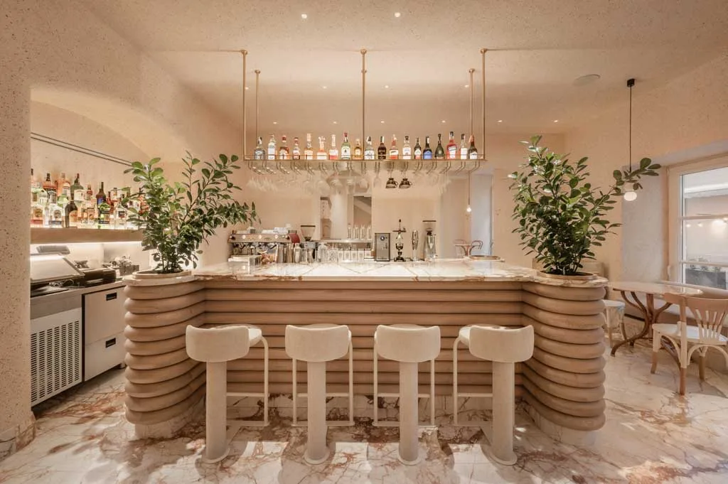 Island bar at Cukiernia pastry shop in Lviv, featuring a rounded design with marble countertops, soft beige tones, and elegant suspended lighting