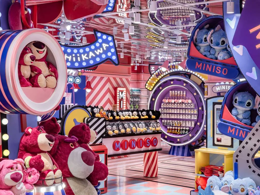 Interni dell’area IP di Miniso Land Shanghai con peluche di personaggi iconici, scaffali colorati e un allestimento ispirato a un parco a tema, tra luci al neon e forme giocose.