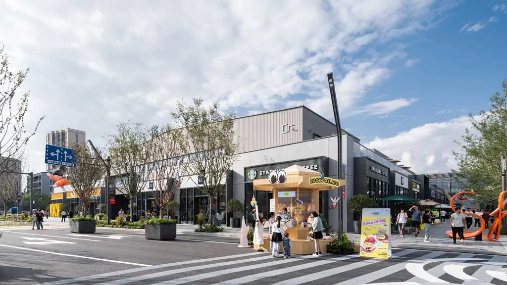 Strada commerciale di SHAOXING PLACE by MixC con negozi moderni, caffetterie e aree pedonali alberate, arricchita da installazioni artistiche e spazi accoglienti per lo shopping e il relax.