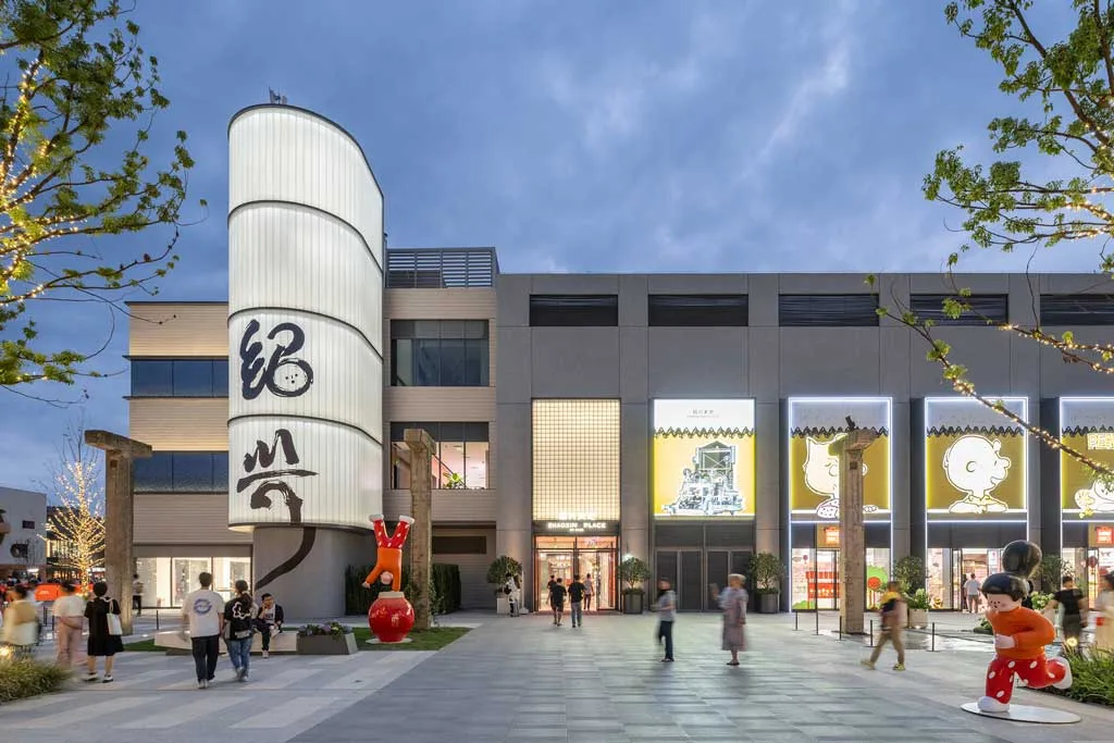 Ingresso di SHAOXING PLACE by MixC con elementi architettonici moderni e illuminazione serale, arricchito da installazioni artistiche e vetrine animate da grafiche ispirate ai Peanuts.