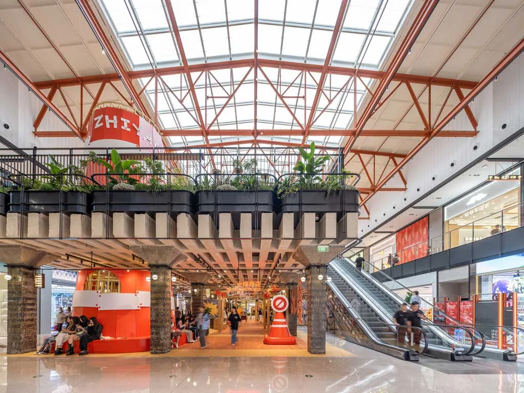  Interno di SHAOXING PLACE by MixC con un'architettura industriale rinnovata, caratterizzata da un tetto vetrato, elementi strutturali in acciaio e spazi commerciali moderni, arricchiti da installazioni artistiche e aree relax.