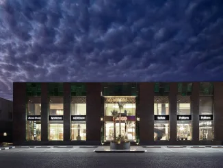 The Oasis Kuwait City – Facciata principale dell'hub di design progettato da Flaviano Capriotti Architetti per Nasco Group. Edificio con ampie vetrate, dettagli in pietra lavica smaltata verde e flagship store di Poliform, Nespresso e altri brand di lusso