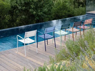 Sedie colorate da esterno disegnate da Patrick Norguet per Vermobil, disposte lungo il bordo di una piscina a sfioro, immerse in un contesto naturale con vegetazione rigogliosa.