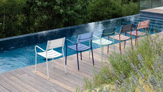 Sedie colorate da esterno disegnate da Patrick Norguet per Vermobil, disposte lungo il bordo di una piscina a sfioro, immerse in un contesto naturale con vegetazione rigogliosa.