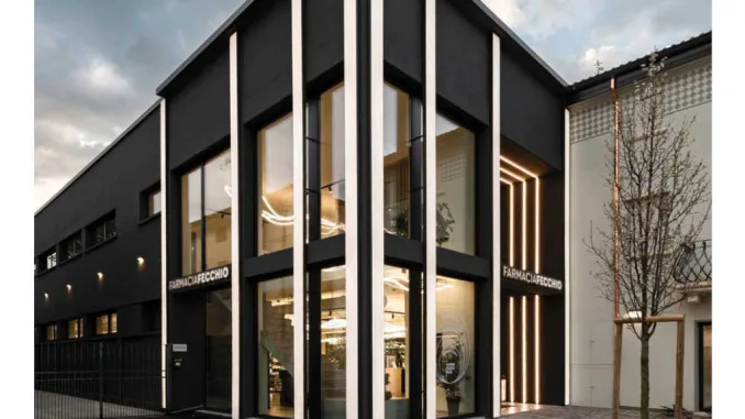 Facciata contemporanea della Farmacia Fecchio con ampie vetrate, illuminazione verticale integrata e rivestimento scuro, progetto di AMlab, foto di Guglielmo Verrienti