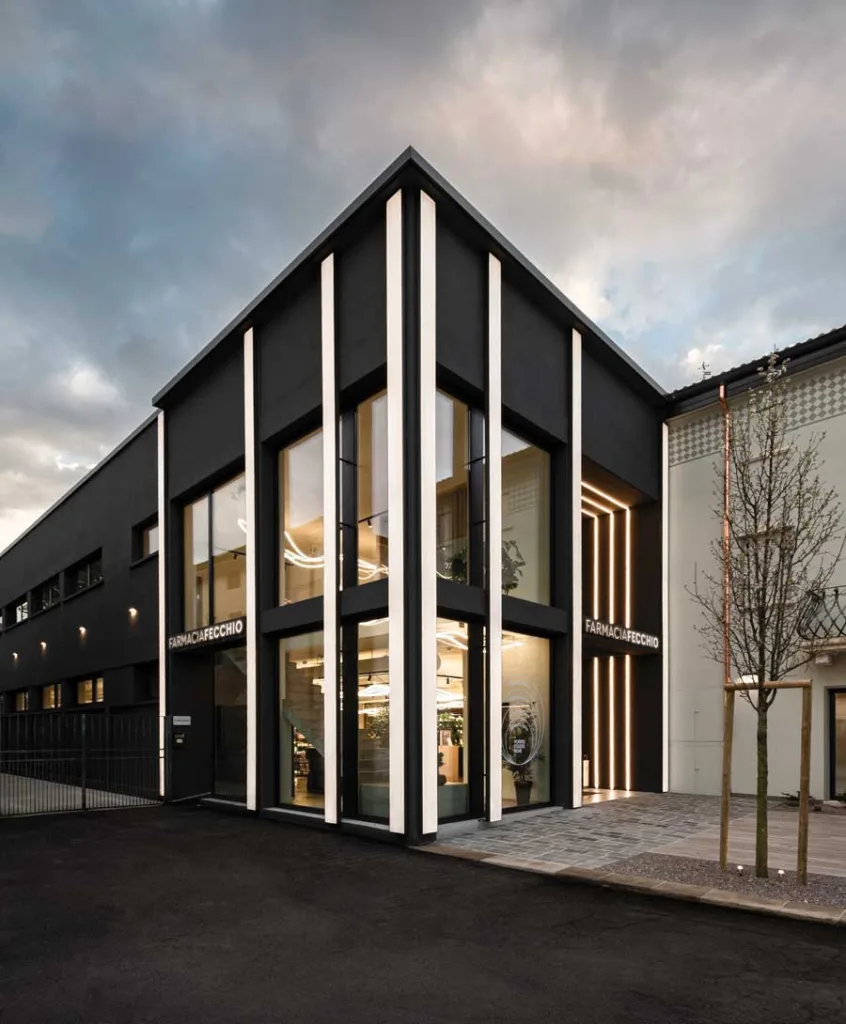 Facciata contemporanea della Farmacia Fecchio con ampie vetrate, illuminazione verticale integrata e rivestimento scuro, progetto di AMlab, foto di Guglielmo Verrienti.
