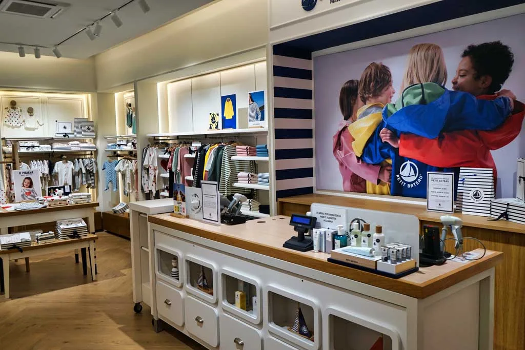 Interno boutique Petit Bateau a Roma con bancone in legno e parete decorata con foto bambini