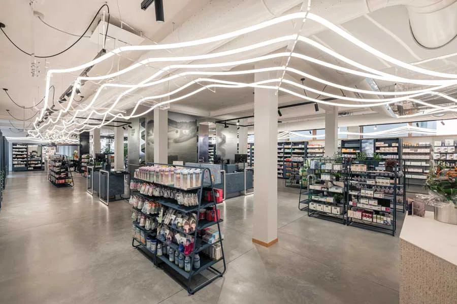 Spazi espositivi della Farmacia Fecchio con layout aperto, scaffalature modulari e soffitto animato da un’illuminazione a onde luminose, progetto di AMlab.