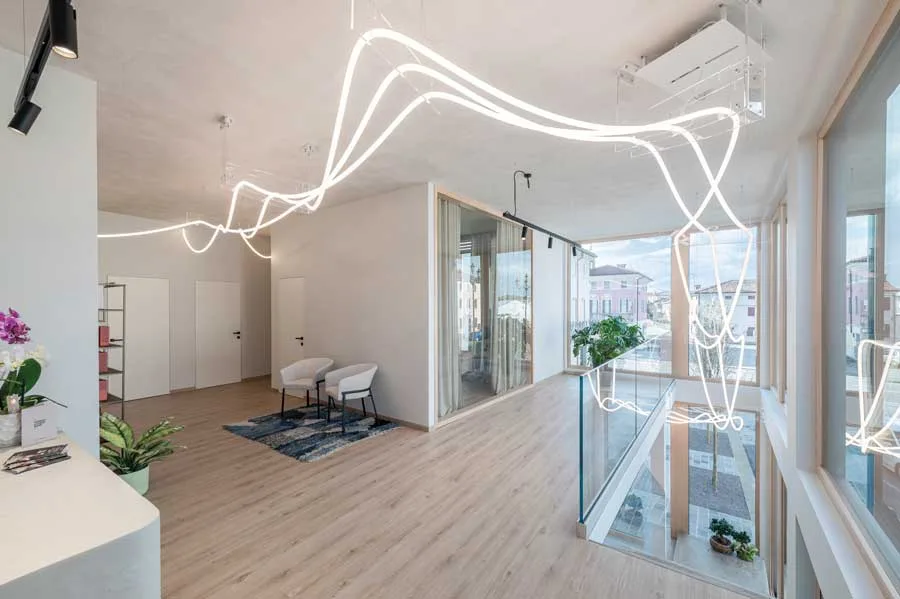 Spazio relax al primo piano della Farmacia Fecchio, progettato da AMlab con ampie vetrate, pavimento in legno e illuminazione LED creativa, esempio di progettazione farmacia contemporanea.