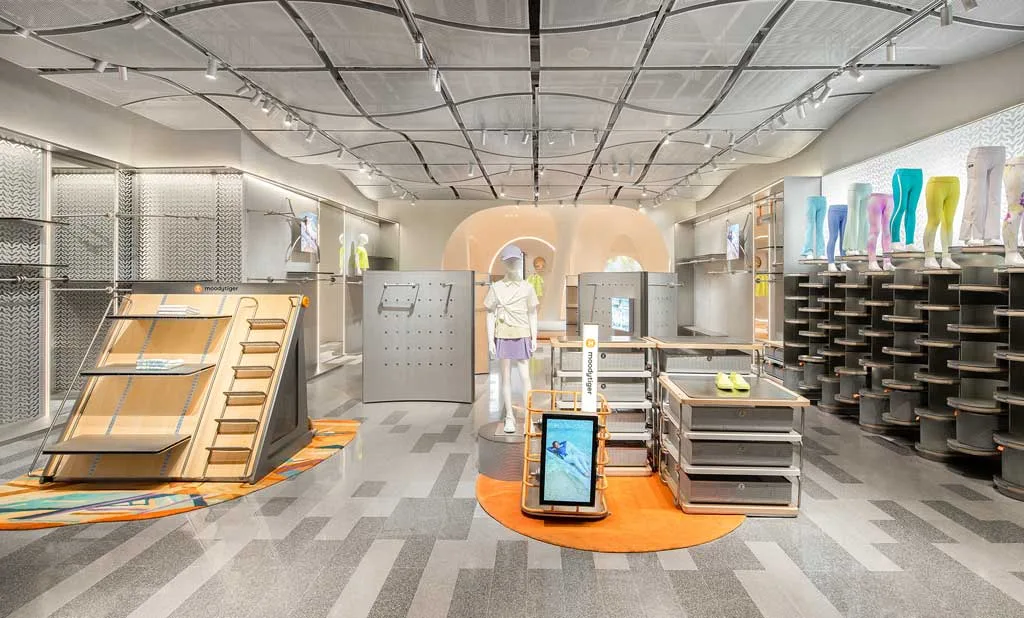 Vista interna del negozio moodytiger con display interattivi, arredi modulari e pareti espositive per abbigliamento sportivo per bambini, progettato da Sò Studio
