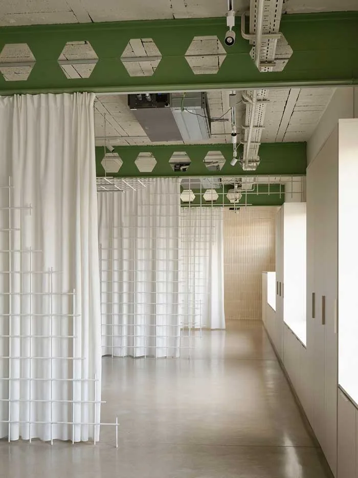 headquarter-di-federico-giner-firmato-clap-studio_700x933 Corridoio del nuovo headquarter di Federico Giner con tendaggi bianchi, strutture metalliche verdi e griglie modulari, progetto firmato da Clap Studio