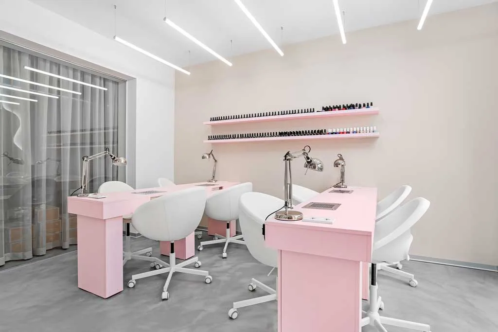 Manicure stations at GxBar salon in Barcelona, with pastel pink furniture, ergonomic white chairs, and a minimal layout curated by Hvylya Design.