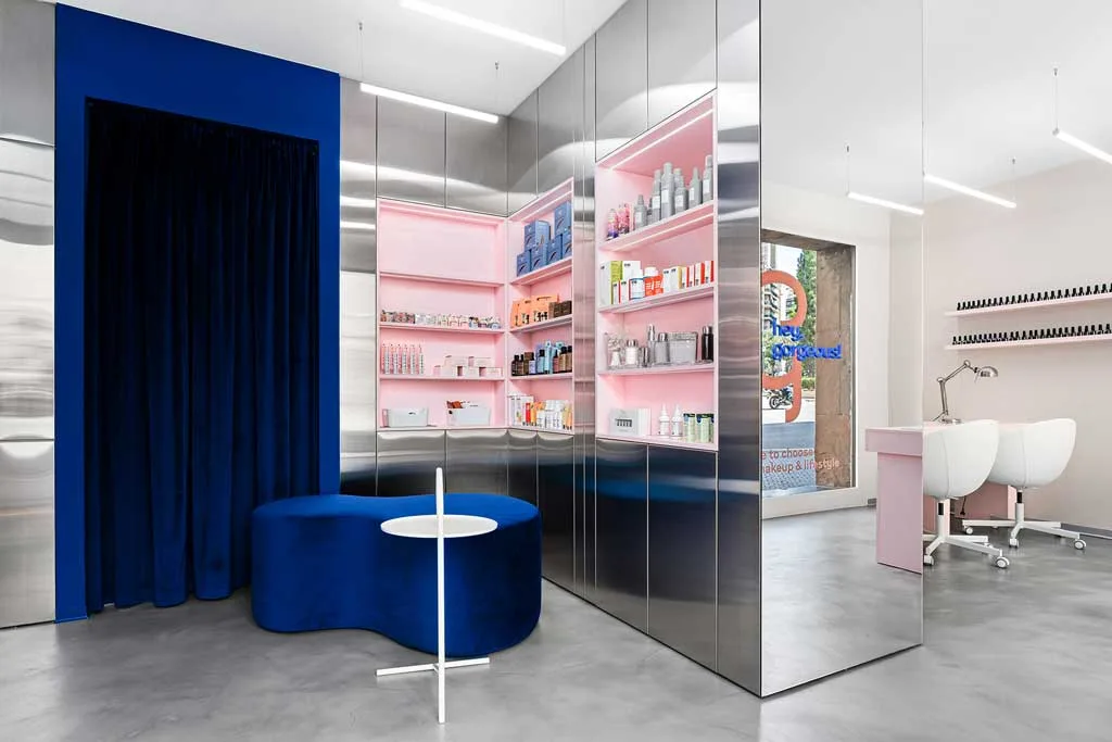 Waiting area of the GxBar beauty salon in Barcelona, featuring custom furnishings, a curved velvet blue seat, and mirrored steel walls — part of the interior design by Hvylya Design.