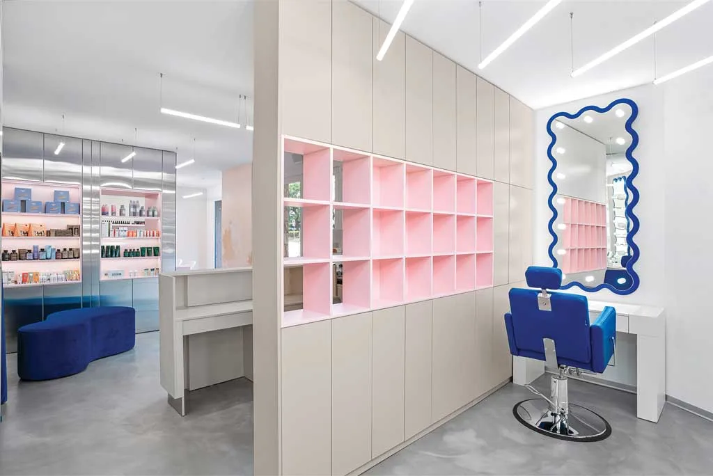 Make-up station at the GxBar salon in Barcelona, with a sculptural backlit mirror, bespoke furnishings, and blue and pink color accents, designed by Hvylya Design.