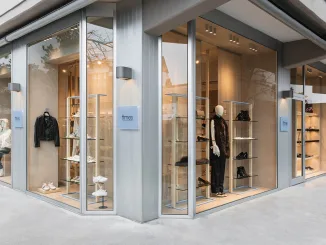 Vista esterna del multibrand store Times a Lignano Sabbiadoro, con vetrine a tutta altezza e manichini che espongono abbigliamento e calzature, progettato con materiali e design eleganti da Moitié Studio