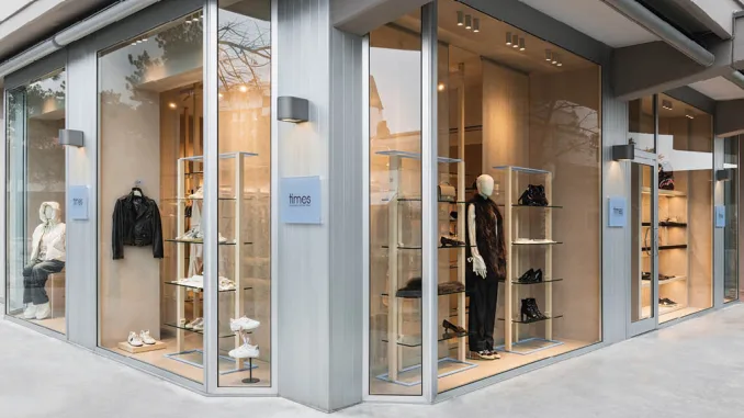 Vista esterna del multibrand store Times a Lignano Sabbiadoro, con vetrine a tutta altezza e manichini che espongono abbigliamento e calzature, progettato con materiali e design eleganti da Moitié Studio
