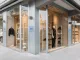 Vista esterna del multibrand store Times a Lignano Sabbiadoro, con vetrine a tutta altezza e manichini che espongono abbigliamento e calzature, progettato con materiali e design eleganti da Moitié Studio