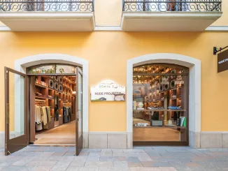 Facciata del flagship store Nude Project a La Roca Village con ingresso vetrato e libreria in legno visibile all'interno, parte del concept "Nude Library".