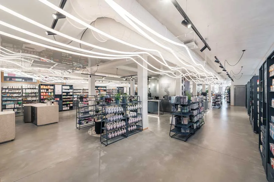 Vista generale della Farmacia Fecchio progettata da AMlab, con layout aperto, espositori modulari e illuminazione LED ondulata, esempio di progettazione farmacia contemporanea.