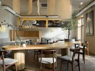 Ampio tavolo conviviale con lampada a sospensione e albero da interno – layout multifunzionale per una caffetteria dall’atmosfera rilassata.
