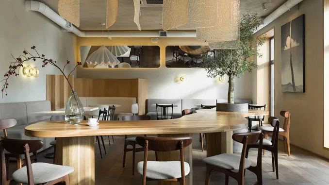 Ampio tavolo conviviale con lampada a sospensione e albero da interno – layout multifunzionale per una caffetteria dall’atmosfera rilassata.