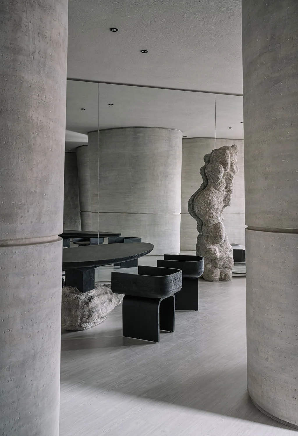 Zona lounge della boutique Zaura con tavolo scultoreo, sedute nere e pareti curve in cemento, esempio di arredamento gioiellerie di design ispirato alla natura
